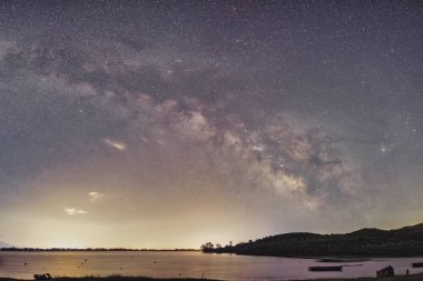 Samanyolu Kerkini Gölü 'nün durgun suları üzerinde parlak bir şekilde parıldıyor. Yalnız bir tekne, doğanın barışçıl kucaklamalarıyla nazikçe sürüklenir. Yıldızların yansıması rüya gibi atmosferi güçlendirir.