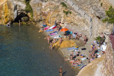 Loutra Edipsou, Evia, Yunanistan 17 Haziran 2025: İnsanlar kayalık oluşumlar ve berrak sularla birlikte manzaralı bir kıyı şeridinde termal yayların ve denizin tadını çıkarıyorlar.