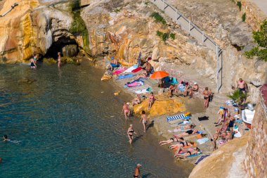 Loutra Edipsou, Evia, Yunanistan 17 Haziran 2025: İnsanlar kayalık oluşumlar ve berrak sularla birlikte manzaralı bir kıyı şeridinde termal yayların ve denizin tadını çıkarıyorlar.
