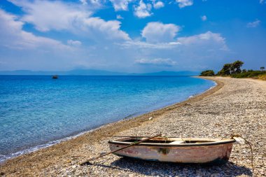Kuzey Evia 'daki çakıl taşı plajı, açık mavi suları, yumuşak kıyı şeridi ve sakin bir yaz gökyüzünün altında kıyıda küçük bir tekne..