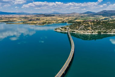 Yunanistan 'daki Polyfytos Gölü' nün eğimli bir köprüsü, mavi suları ve manzaralı dağları var. Doğayı, mimariyi ve kırsal cazibeyi harmanlayan huzurlu bir manzara.