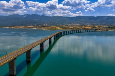 Yunanistan 'daki Polyfytos Gölü' nün eğimli bir köprüsü, mavi suları ve manzaralı dağları var. Doğayı, mimariyi ve kırsal cazibeyi harmanlayan huzurlu bir manzara.