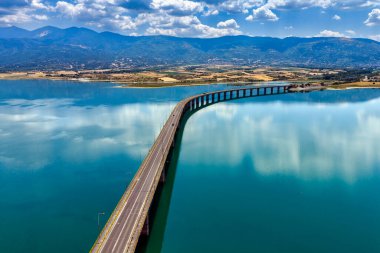 Yunanistan 'daki Polyfytos Gölü' nün eğimli bir köprüsü, mavi suları ve manzaralı dağları var. Doğayı, mimariyi ve kırsal cazibeyi harmanlayan huzurlu bir manzara.