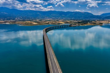 Yunanistan 'daki Polyfytos Gölü' nün eğimli bir köprüsü, mavi suları ve manzaralı dağları var. Doğayı, mimariyi ve kırsal cazibeyi harmanlayan huzurlu bir manzara.