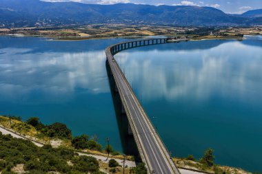 Yunanistan 'daki Polyfytos Gölü' nün eğimli bir köprüsü, mavi suları ve manzaralı dağları var. Doğayı, mimariyi ve kırsal cazibeyi harmanlayan huzurlu bir manzara.