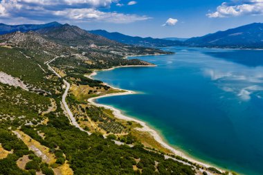 Yunanistan 'daki Polyfytos Gölü' nün sakin hava manzarası, yemyeşil tepeler ve sakin mavi sularla çevrili. Seyahat ve doğa severler için mükemmel huzurlu doğal bir manzara.