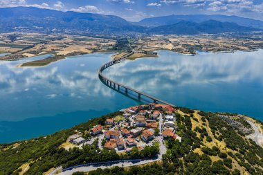 Yunanistan 'daki Polyfytos Gölü' nün eğimli bir köprüsü, mavi suları ve manzaralı dağları var. Doğayı, mimariyi ve kırsal cazibeyi harmanlayan huzurlu bir manzara.