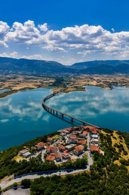 Yunanistan 'daki Polyfytos Gölü' nün eğimli bir köprüsü, mavi suları ve manzaralı dağları var. Doğayı, mimariyi ve kırsal cazibeyi harmanlayan huzurlu bir manzara.