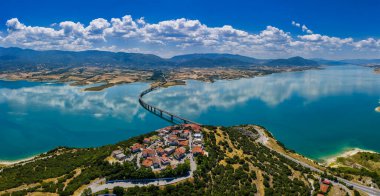 Yunanistan 'daki Polyfytos Gölü' nün eğimli bir köprüsü, mavi suları ve manzaralı dağları var. Doğayı, mimariyi ve kırsal cazibeyi harmanlayan huzurlu bir manzara.