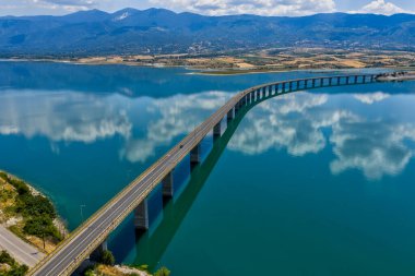 Yunanistan 'daki Polyfytos Gölü' nün eğimli bir köprüsü, mavi suları ve manzaralı dağları var. Doğayı, mimariyi ve kırsal cazibeyi harmanlayan huzurlu bir manzara.