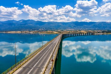 Yunanistan 'daki Polyfytos Gölü' nün eğimli bir köprüsü, mavi suları ve manzaralı dağları var. Doğayı, mimariyi ve kırsal cazibeyi harmanlayan huzurlu bir manzara.