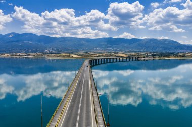 Yunanistan 'daki Polyfytos Gölü' nün eğimli bir köprüsü, mavi suları ve manzaralı dağları var. Doğayı, mimariyi ve kırsal cazibeyi harmanlayan huzurlu bir manzara.