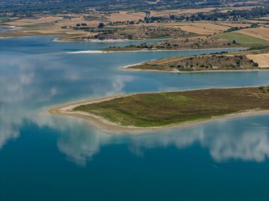 Yunanistan 'daki Polyfytos Gölü' nün sakin hava manzarası, yemyeşil tepeler ve sakin mavi sularla çevrili. Seyahat ve doğa severler için mükemmel huzurlu doğal bir manzara.