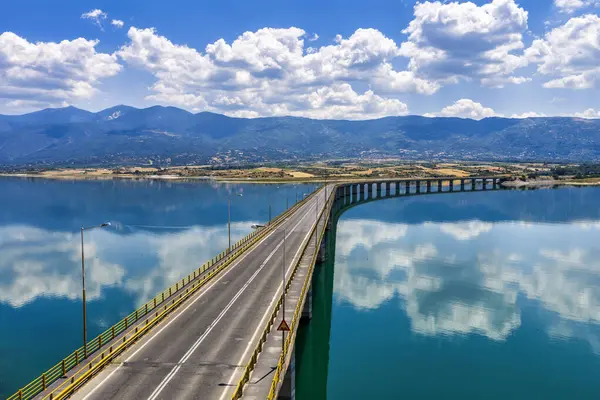 Yunanistan 'daki Polyfytos Gölü' nün eğimli bir köprüsü, mavi suları ve manzaralı dağları var. Doğayı, mimariyi ve kırsal cazibeyi harmanlayan huzurlu bir manzara.