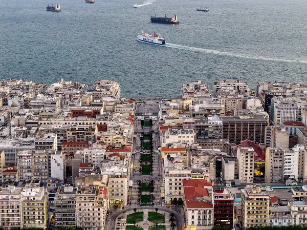 Selanik, Yunanistan 3 Ağustos 2025. Pembe gökyüzü, şehir mimarisi, termaik körfezdeki gemiler ve yeşil park alanlarıyla şehir merkezinin hava aracı görüntüsü.