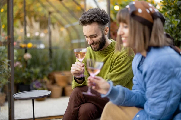 若いスタイリッシュなカップルが一緒にぶらついて 裏庭に座っている間にワインを話し 飲みます 男と女は屋外の居心地の良い雰囲気で夜を過ごす — ストック写真