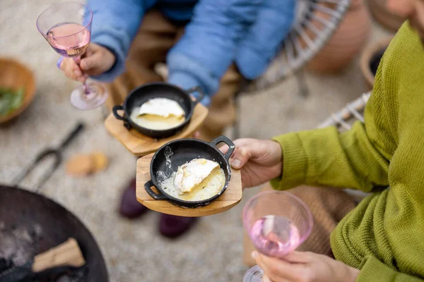 年轻夫妇一起吃饭 一边吃热奶酪和面包 一边喝酒 同时坐在花园的炉边生火 在盘子里的奶酪特写 — 图库照片