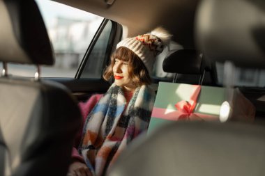 Tatil için giyinmiş genç bir kadın güzel paketlenmiş Noel hediyeleriyle arka koltukta araba kullanıyor. Kış tatili, hazırlık ve alışveriş beklentisiyle