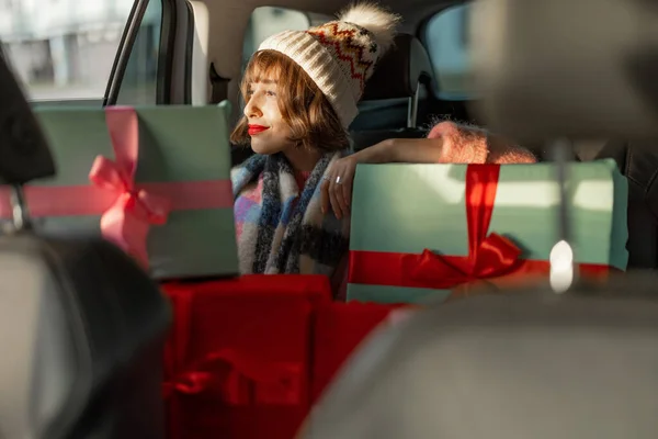 身着节日服装的年轻女子坐在后座上开车 带着包装精美的圣诞礼物 为迎接寒假 准备和购物 — 图库照片