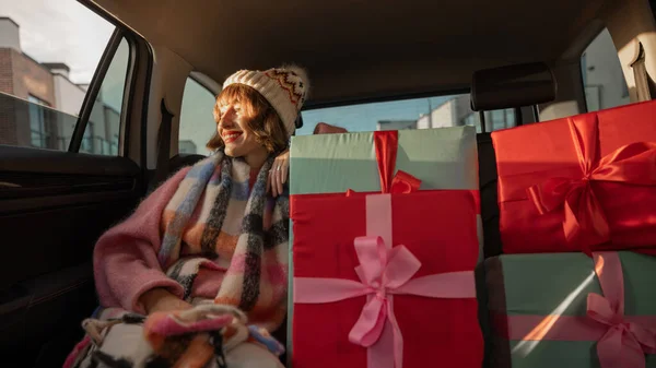 美しい包まれたクリスマスプレゼントと後部座席の車の中で休日のドライブのために身を包んだ若い女性 冬の休日やショッピングを期待して 広角撮影 — ストック写真
