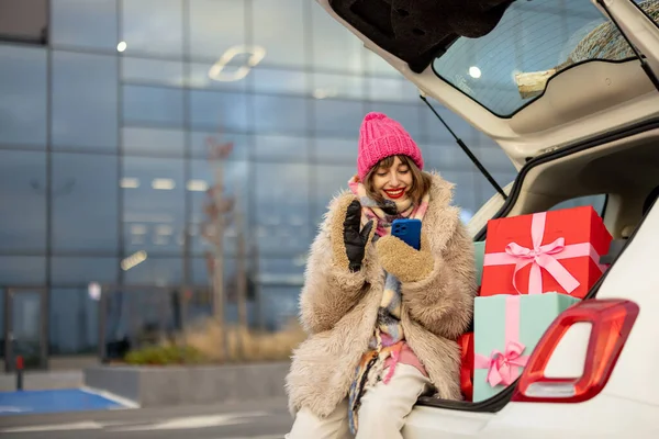 年轻快乐的女人坐在满是圣诞礼物的汽车行李箱里打电话 在购物中心里过冬购物 新年心情和购物理念 — 图库照片