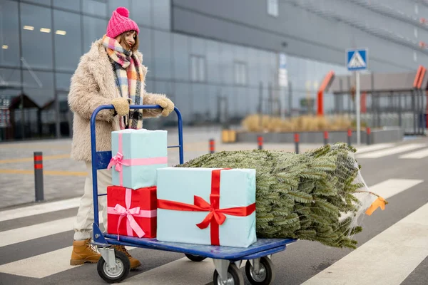 Γυναίκα Σπρώχνει Τρόλεϊ Ψώνια Γεμάτη Δώρα Και Χριστουγεννιάτικο Δέντρο Μπροστά — Φωτογραφία Αρχείου