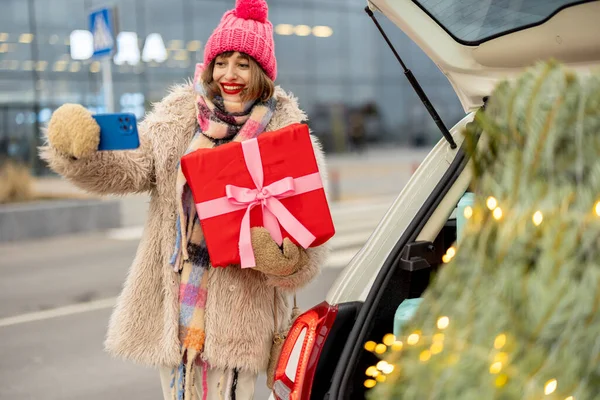 穿着冬装的女人在网上聊天 在购物中心购物过冬 站在靠近礼品盒的地方 刚刚在户外买了一棵圣诞树 — 图库照片