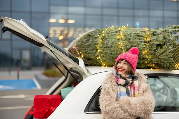 快乐的女人梦想着一个快乐的假期 而站在汽车旁边 上面挂着圣诞树 女孩在商场购物过年 — 图库照片