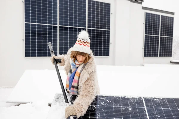 女性は家の屋根の上で冬に発電するために雪から太陽電池パネルをきれいにします エネルギー自立と持続可能性の概念 — ストック写真