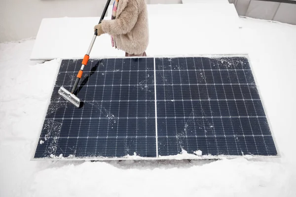女性は家の屋根の上で冬に発電するために雪から太陽電池パネルをきれいにします エネルギー自立と持続可能性の概念 — ストック写真