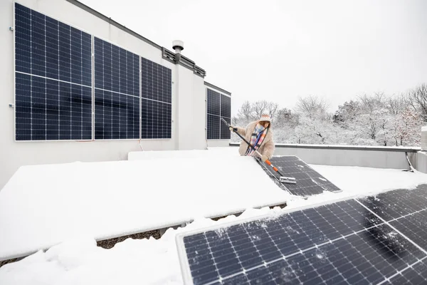 女人从雪地上清理太阳能电池板 在自家屋顶上为大自然发电 能源独立和可持续性概念 广角镜 — 图库照片