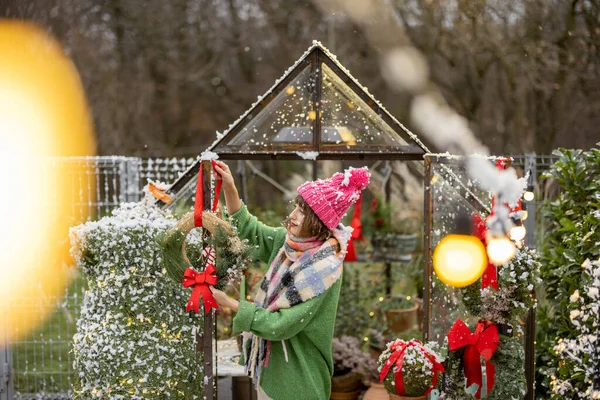 年轻女人用新年花圈装饰温室 准备在后院过冬 节日气氛及装饰的概念 — 图库照片