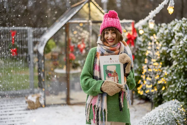 一位年轻女子的画像 她在雪地的后院拿着一本杂志 上面有新年的封面 准备过冬 — 图库照片