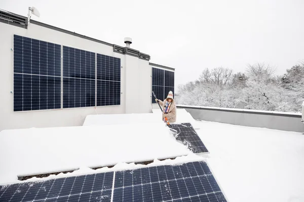 女性は雪から太陽光パネルをきれいにして 自然の上で彼女の家の屋根の上に冬に電力を生産する エネルギー自立と持続可能性の概念 広角ビュー — ストック写真