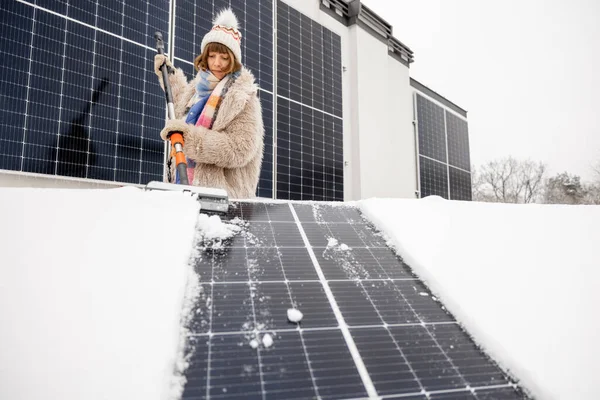 Woman cleans solar panels from snow to produce power in winter on the roof of her house. Energy independence and sustainability concept