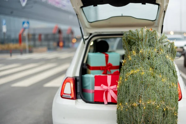 屋外のギフトボックスでいっぱいの車のトランクの近くのガーランドで飾られたクリスマスツリーを包んだ 冬休み ショッピングのコンセプト — ストック写真