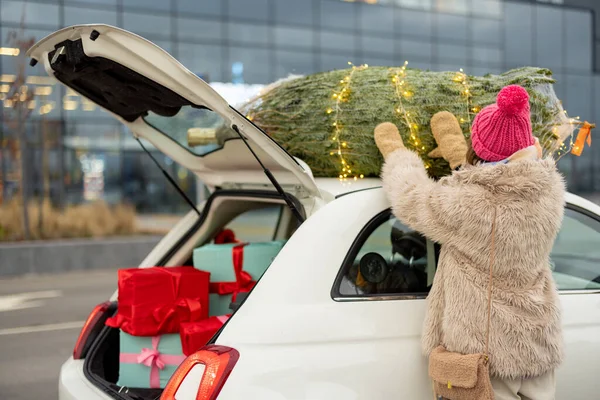在购物中心购物的时候 一位年轻的女士用绳子把圣诞树绑在她的车顶上 寒假和购物的概念 — 图库照片