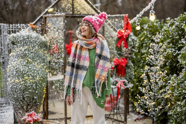 一个戴着帽子和围巾的年轻女子在装饰精美的后院享受降雪的画像 寒假和节日气氛的概念 — 图库照片
