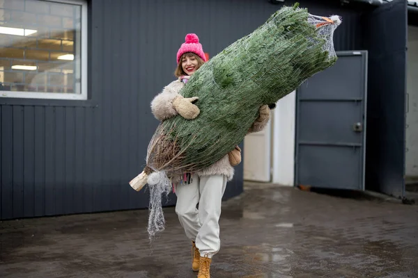 年轻女子带着包裹着的圣诞树 从邮局从网上商店送货出去 冬季假期派递和网上购物的概念 — 图库照片