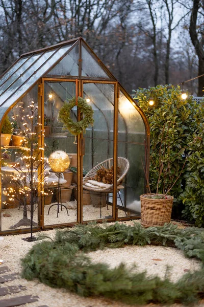 Beautiful backyard with vintage glasshouse and Christmas wreath decorated with garlands during winter time. Concept of coziness and decoration on winter holidays