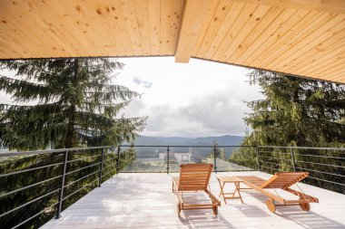 Doğada ahşap şezlonglu geniş bir teras. Çam ağaçları ve dağlar manzaralı.