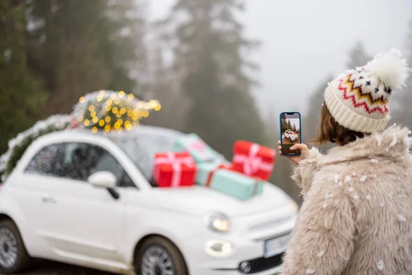 Жінка Робить Фотографію Телефоні Красивого Автомобіля Прикрашеного Подарунками Ялинкою Даху — стокове фото