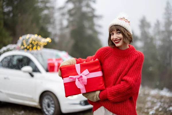 스웨터를 모자를 여성의 모습은 상자를 있으며 산에서 크리스마스 트리로 장식된 — 스톡 사진