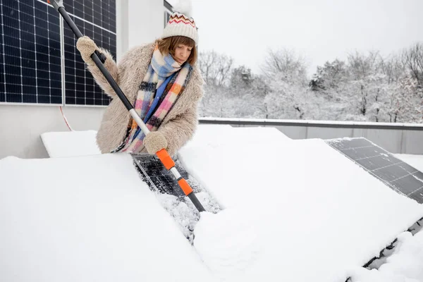 女人在自家屋顶上清扫雪地上的太阳能电池板以产生电力 能源独立和可持续性概念 — 图库照片