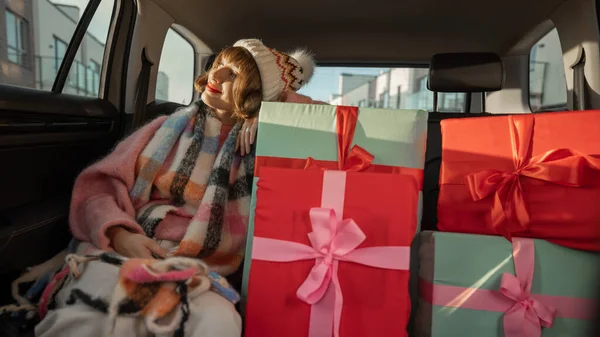 身着节日服装的年轻女子坐在后座上开车 带着包装精美的圣诞礼物 为了迎接寒假和购物 广角镜头 — 图库照片