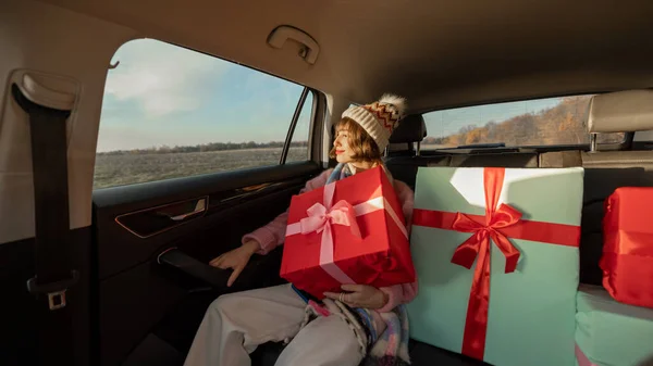 身着节日服装的年轻女子坐在后座上开车 带着包装精美的圣诞礼物 为了迎接寒假和购物 广角镜头 — 图库照片
