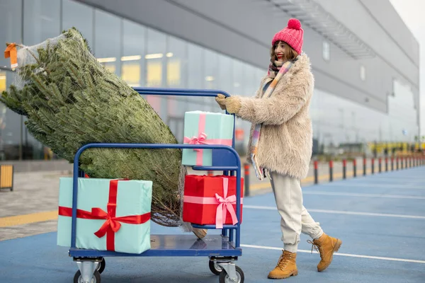 Γυναίκα Σπρώχνει Τρόλεϊ Ψώνια Γεμάτη Δώρα Και Χριστουγεννιάτικο Δέντρο Στο — Φωτογραφία Αρχείου