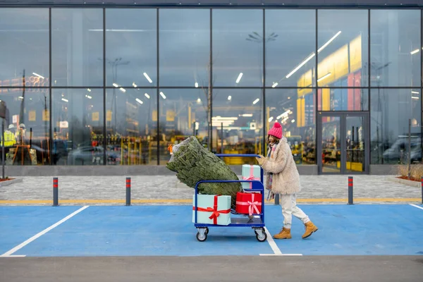 Mujer Empujando Carrito Lleno Regalos Árbol Navidad Frente Centro Comercial — Foto de Stock
