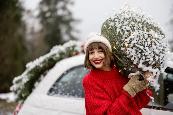 雪の日に山の中で車で旅行クリスマスツリーラップと女性の肖像画 幸せな冬の休暇のための準備の概念 車の後ろにプレゼントや花輪で飾られた — ストック写真