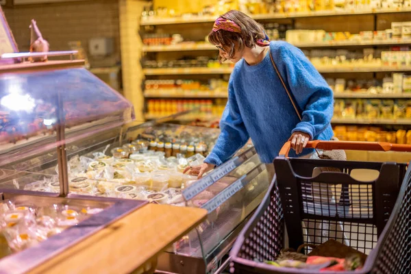 若い女性は スーパーマーケットでのショッピングトロリーと立ってチーズを購入 店内における乳製品の買い物の概念 — ストック写真